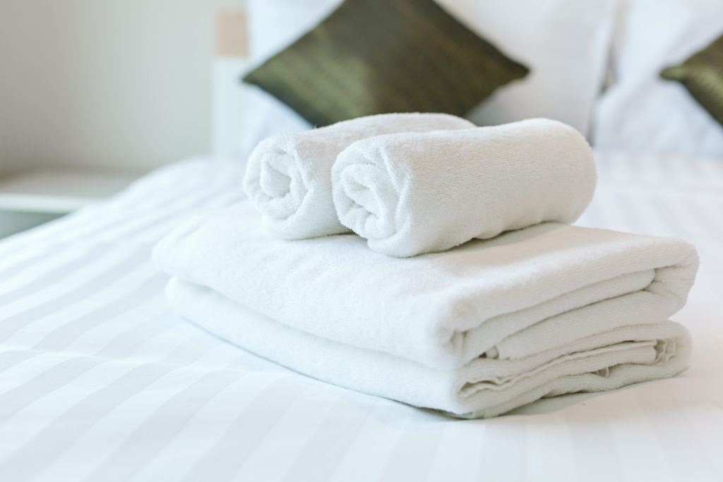 Weiße Flachwäsche auf Hotelbett, Handtücher und Kissenbezüge