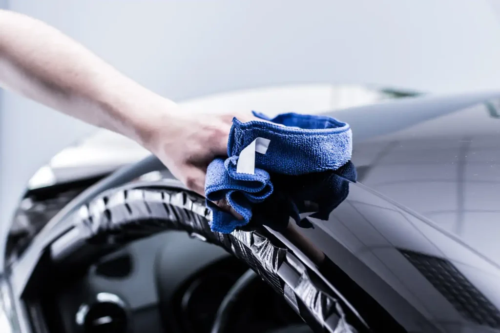 Ein Auto wird per Hand mit einem blauen Mikrofaser Putztuch auf Hochglanz poliert