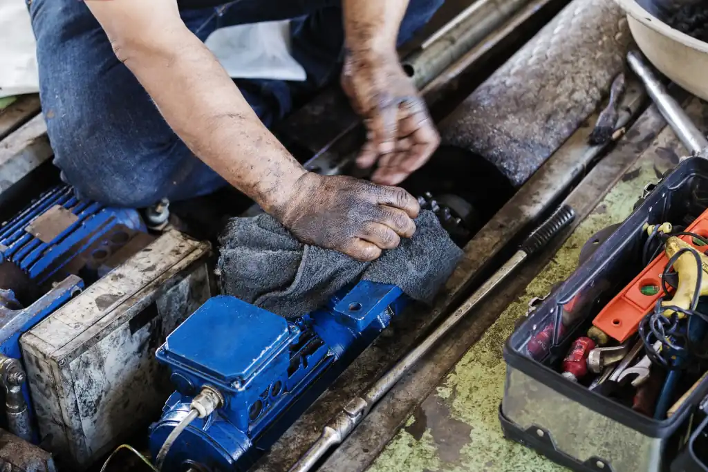 KFZ Mechaniker reinigt den oelverschmierten Motor eines Autos mit gemieteten Putztuechern