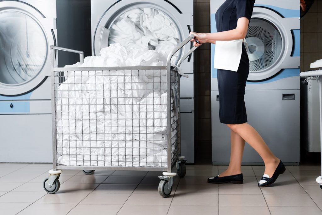 Hausangestellte schiebt Waeschewagen vor Waschmaschinen